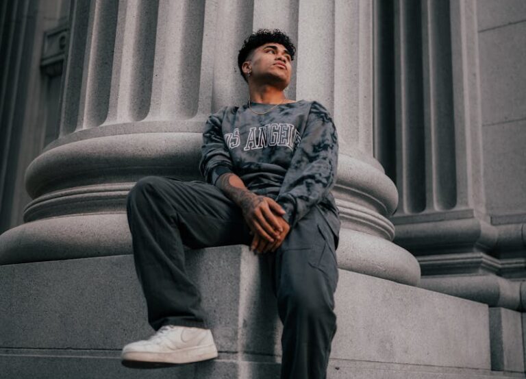 stylowy mężczyzna siedzący przy klasycznej kolumnie ubrany w bluzę